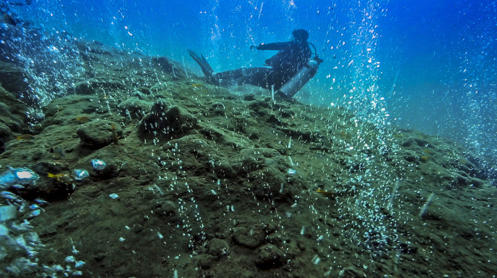 Scuba diver relaxing in hot water bubbles at underwater volcano,